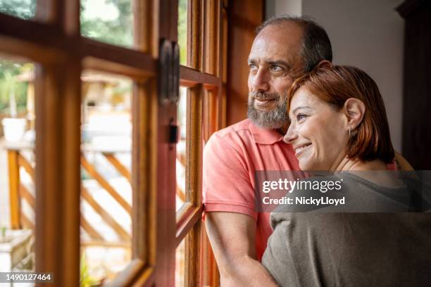 beautiful mature couple standing by bedroom window - olhar através da janela imagens e fotografias de stock
