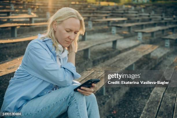 blond hair woman with headphones with a smartphone in her hands - mid adult stock pictures, royalty-free photos & images