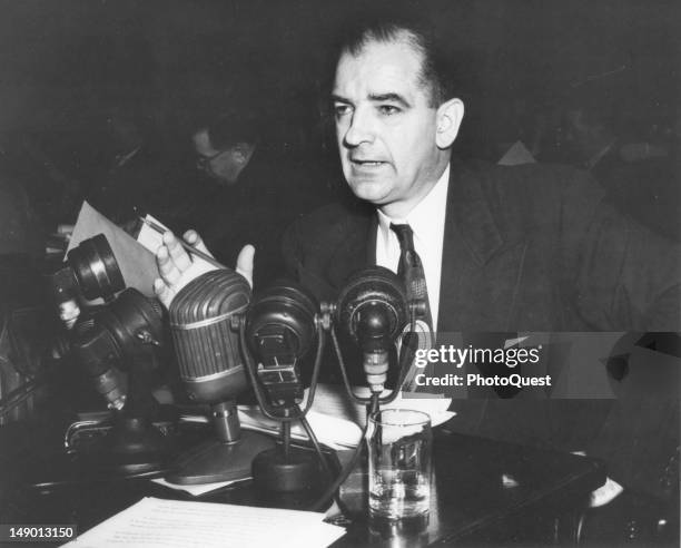 American politian US Senator Joseph R. McCarthy speaks from behind a bank of microphones, mid 20th century.