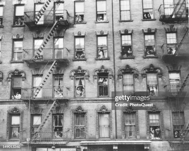 View of the inhabitants of a tenament house as they look out from their windows, Newark, New Jersey, early 20th century. The store on the ground...