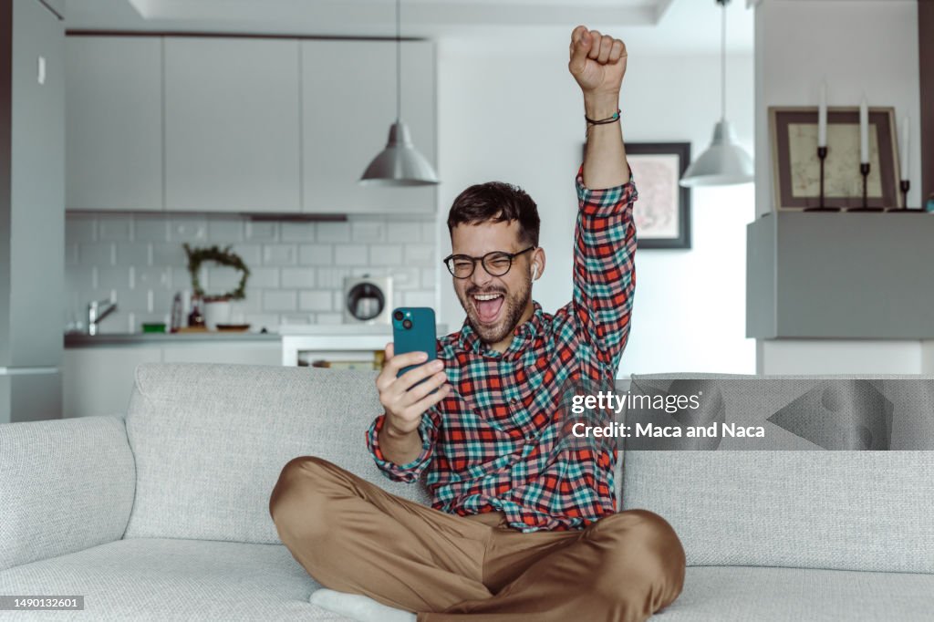 Ein lächelnder Mann, der ein Handy hält und Erfolge feiert