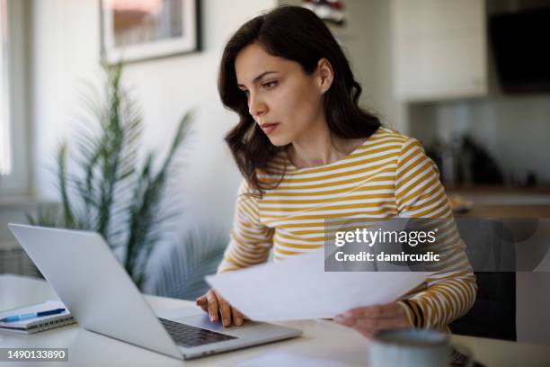 jeune femme sérieuse travaillant à la maison - femme facture photos et images de collection