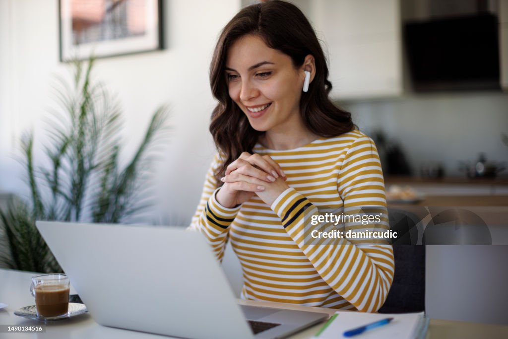 Young smiling woman with bluetooth headphones having video call at home