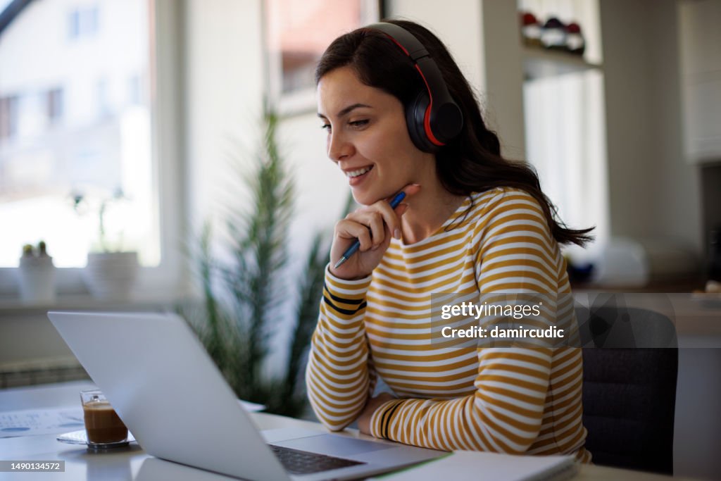 Junge Frau mit Bluetooth-Kopfhörern, die zu Hause an ihrem Laptop arbeiten