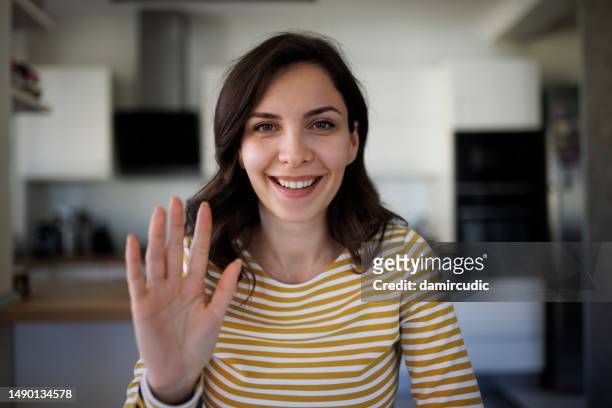 junge lächelnde frau winkt mit der hand beim videoanruf im home office - waving hands goodbye stock-fotos und bilder