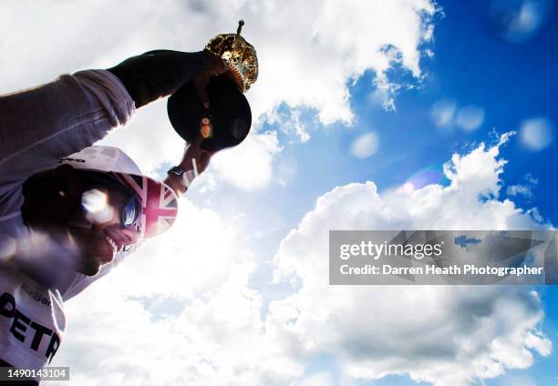 Photographed in back lit light, lens flare inducing light under a cloudscape sky, smiling British Mercedes-AMG Formula One racing team racing driver...