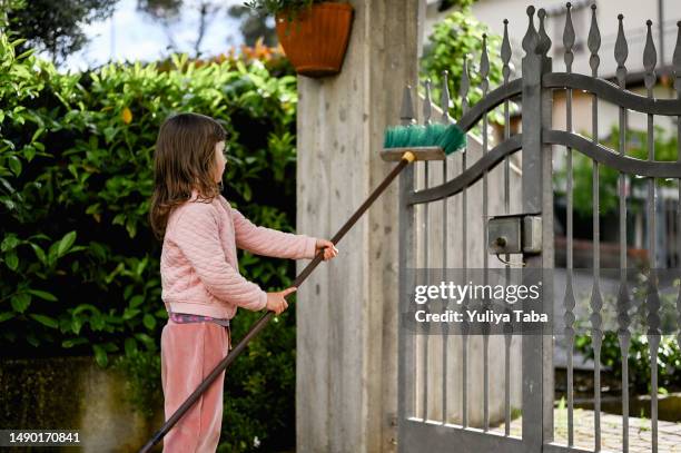 petite fille aidant à nettoyer la porte dans le jardin avec un balai. - portail photos et images de collection