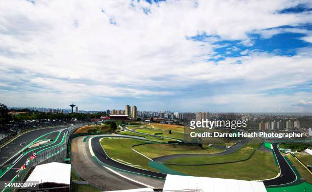 Photographed from an elevated position, Formula One racing cars driving around the circuit in front of houses and apartments in a neighbouring favela...