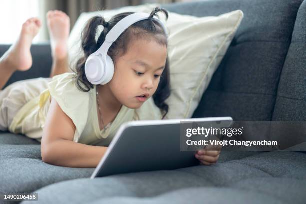 young girl on sofa using digital tablet and headphones - herne hill stock pictures, royalty-free photos & images