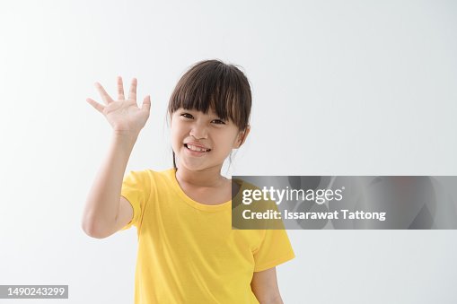 girl says hello, waves hand and smiles happy at you, stands over white background