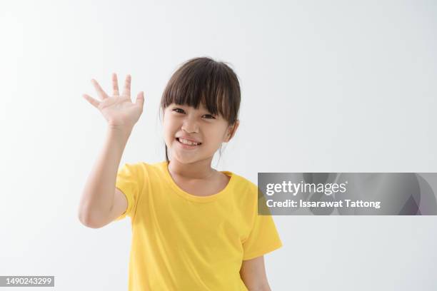 girl says hello, waves hand and smiles happy at you, stands over white background - child waving stock pictures, royalty-free photos & images