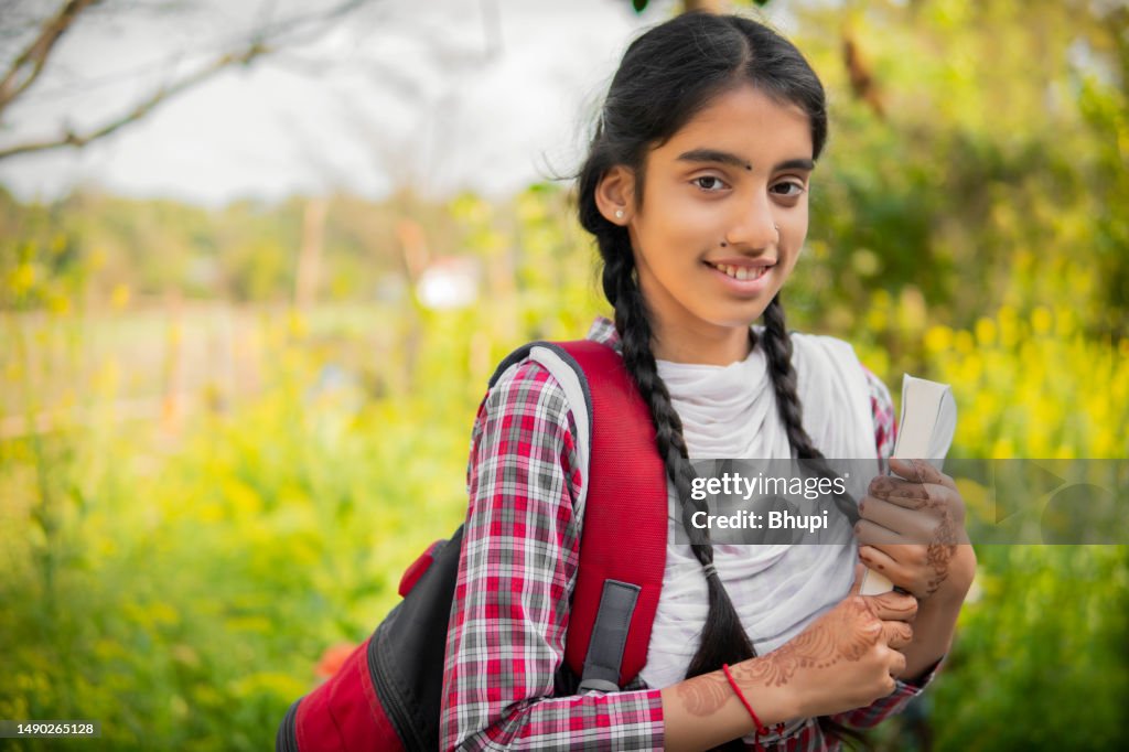 Portrait of Indian schoolgirl in uniform holding a book and backpack.