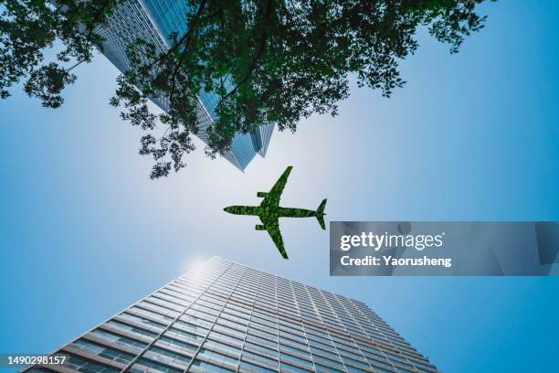 low angle view of green airplane flying over business office building - clear sky plane stock pictures, royalty-free photos & images