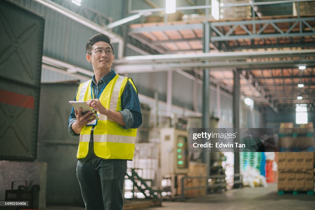 Trabalhador de armazém chinês asiático satisfeito tirando estoque olhando para longe com tablet digital no armazém logístico