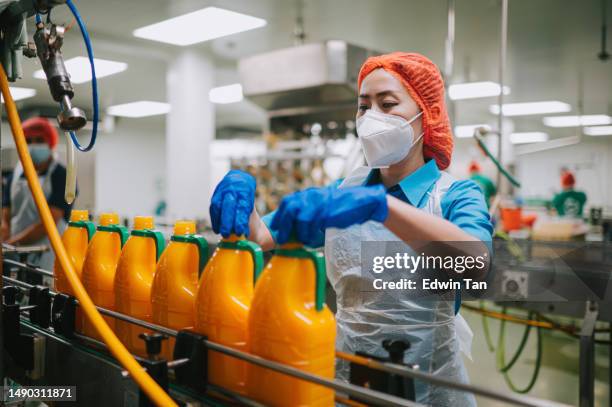 trabajadora asiática china de una fábrica de jugos aprieta la tapa de la botella en la línea de producción - food and drink industry fotografías e imágenes de stock