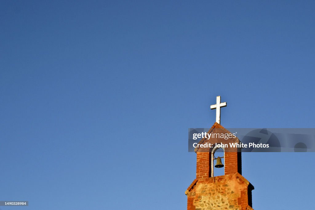 Cross and bell on the top of a church steeple.