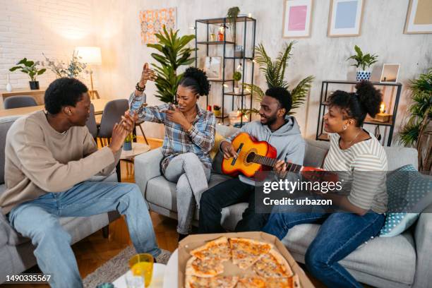 famiglia nera che suona una chitarra acustica e canta in salotto - plucking an instrument foto e immagini stock