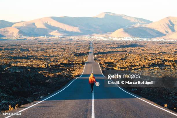 woman boldly walking on a long straight road in lanzarote, spain - lanzarote stock pictures, royalty-free photos & images