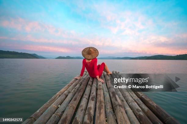 woman with red dress and traditional hat sitting on a wooden raft - philippinische kultur stock-fotos und bilder