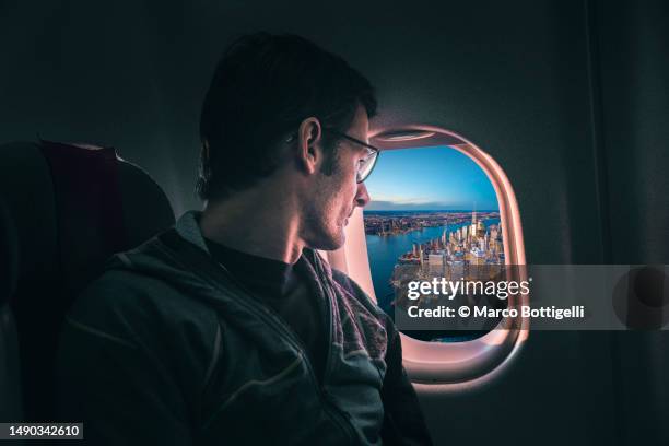 man looking out the airplane window at new york city at dusk - raamplaats stockfoto's en -beelden