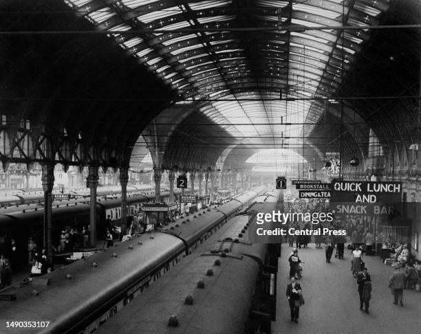 Passengers and commuters alike on the platforms as trains wait to depart from Paddington Railway Station in London, England, 1950. Signs for the...