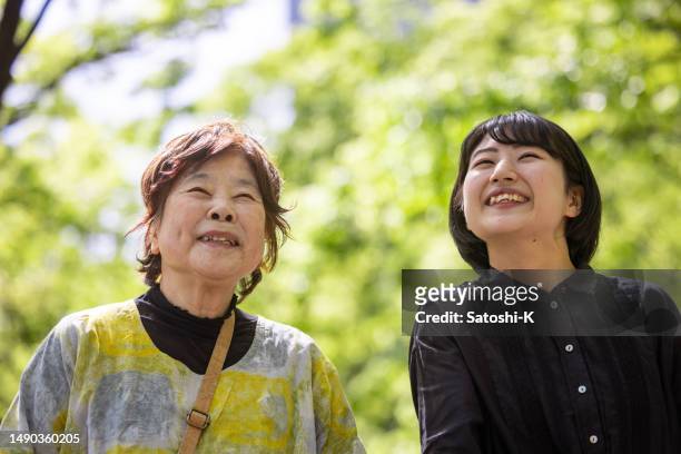 young woman walking and talking with her grandmother on a street lined with trees - looking up together - young woman and senior lady in a park stock pictures, royalty-free photos & images