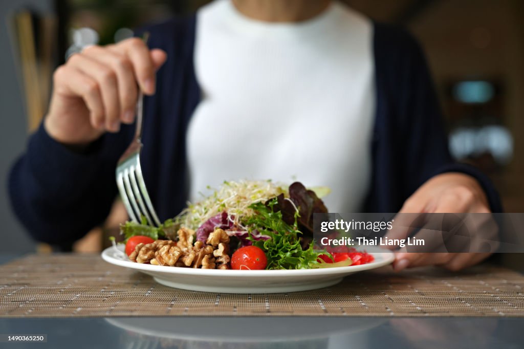 Cropped image of woman having healthy green salad with alfalfa sprouts, cherry tomatoes, walnuts, leafy vegetables, olives, and salad dressing.