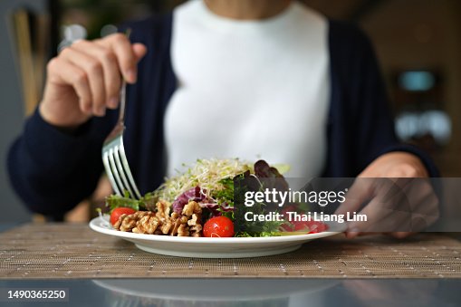 Cropped image of woman having healthy green salad with alfalfa sprouts, cherry tomatoes, walnuts, leafy vegetables, olives, and salad dressing. Cropped image of woman having healthy green salad with alfalfa sprouts, cherry tomatoes, walnuts, leafy vegetables, olives, and salad dressing.