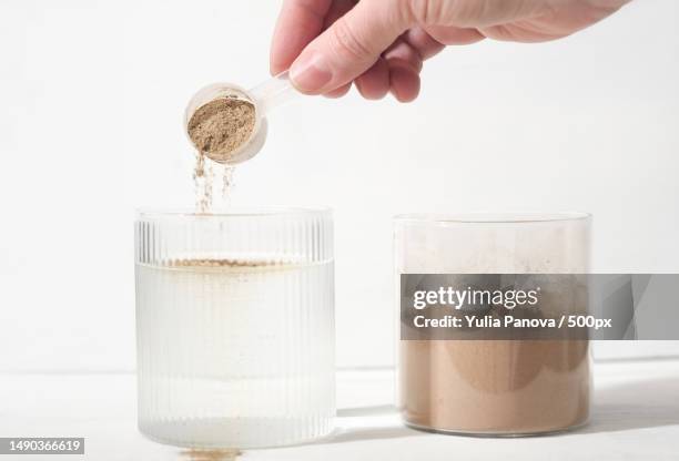 woman pouring plant based protein powder into a glass of water plant protein as food supplement - protein powder stock-fotos und bilder