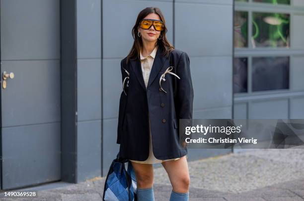 Amelie Stanescu wears navy blazer with ribbon details by Munthe, oversized shirt by Munthe, knee high denim boots vintage, Tom Ford sunglasses, denim...