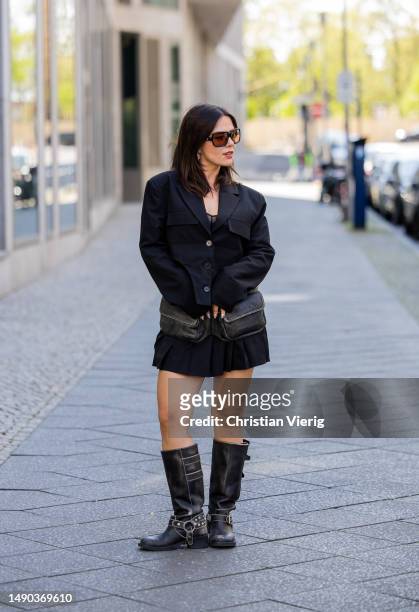 Amelie Stanescu wears black cropped blazer by Lumia, pleated mini skirt by Lumia, belt pocket bag by Mango, sunglasses by Miu Miu, buckle biker boots...