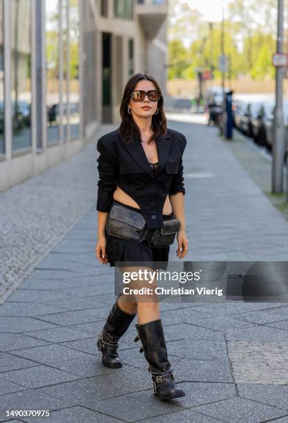 Amelie Stanescu wears black cropped blazer by Lumia, pleated mini skirt by Lumia, belt pocket bag by Mango, sunglasses by Miu Miu, buckle biker boots...