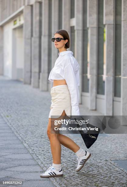 Jacqueline Zelwis wears white cropped ONWEEKENDS button shirt, LeGer skirt in beige, Adidas sneakers, Gucci bag in black, Isabel Marant sunglasses,...