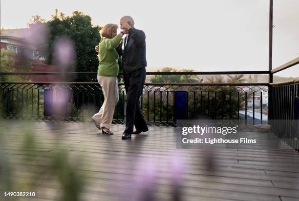 loving senior couple affectionately dances together on patio with flowers in the foreground - memorial garden stock pictures, royalty-free photos & images