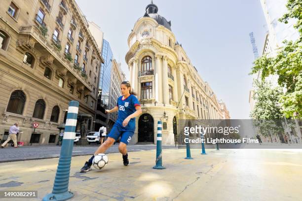 agile woman soccer player athletically kicks ball down picturesque sidewalks of santiago, chile - midfielder soccer player stock pictures, royalty-free photos & images