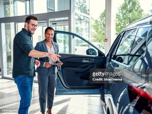 saleswoman helping the male customer to choose a new car - car sales man stock pictures, royalty-free photos & images