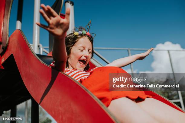 a delighted child on a slide in a park on a sunny day - kid sliding stock pictures, royalty-free photos & images