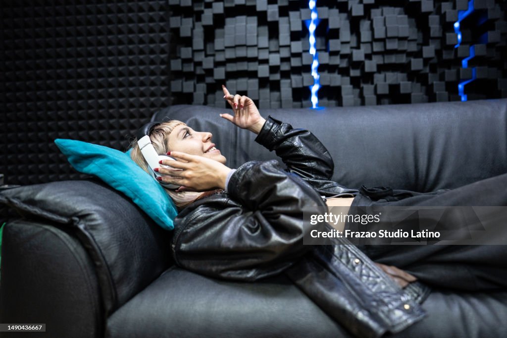 Singer young woman listening music lying on sofa in the recording studio