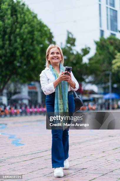 mujer de 50 a 55 años, en la calle con el celular en la mano - 50 54 years fotografías e imágenes de stock