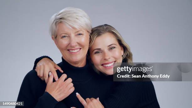 portrait of a senior woman with her adult daughter in a studio with love, care and happiness. bonding, smile and happy elderly lady in retirement hugging her female child isolated by gray background. - model smile stockfoto's en -beelden