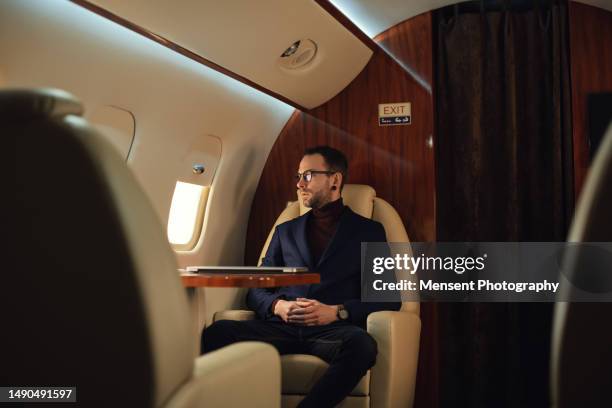 elegant businessman sits in a private airplane jet, looking through windows before take-off - first class flight stock pictures, royalty-free photos & images