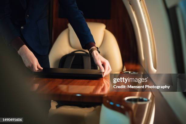 elegant businessman pulls out a laptop to work from his backpack and places it on the table in a private airplane jet - vip travel stock pictures, royalty-free photos & images