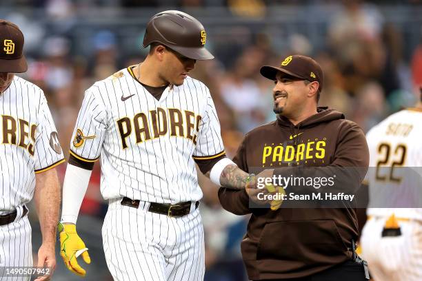 Trainer Ricky Huerta assesses Manny Machado of the San Diego Padres after he was hit by a pitch on the wrist during the second inning of a game...