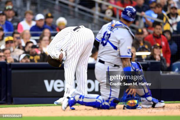 Manny Machado of the San Diego Padres leans over in pain after being hit on the wrist by a pitch as Salvador Perez of the Kansas City Royals looks on...