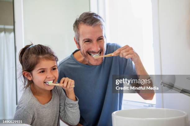 père et fille souriant au miroir tout en se brossant les dents - se brosser les dents photos et images de collection