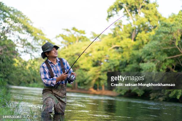man fly fishing at tranquil green river - ankle deep in water - fotografias e filmes do acervo