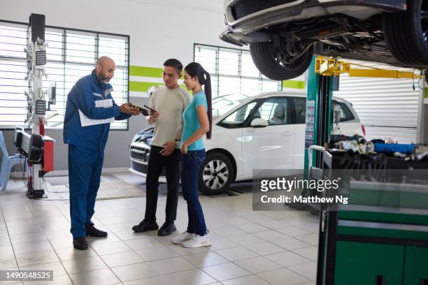 young asian couple makes payment to asian car mechanic in a car workshop - asian couple garage car stock pictures, royalty-free photos & images