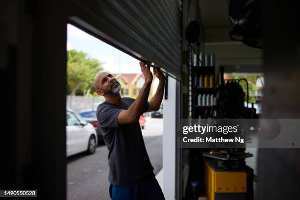 asian male mechanic opening shutter door to car workshop - oficina automóvel imagens e fotografias de stock