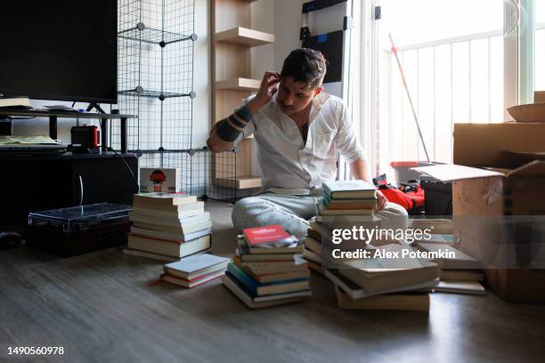 bücher aussuchen und entrümpeln. hispanoamerikaner zieht in ein neues haus, packt aus und räumt das wohnzimmer auf, setzt sich auf den boden am hellen fenster - entrümpeln stock-fotos und bilder