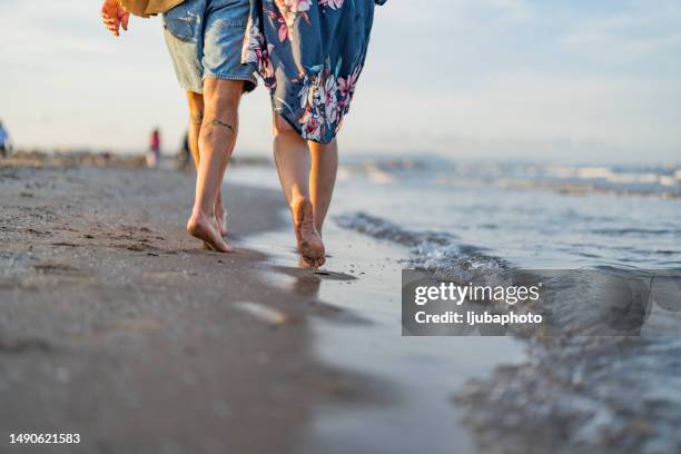 pareja dando un paseo junto al mar en una playa de arena - borde del agua fotografías e imágenes de stock